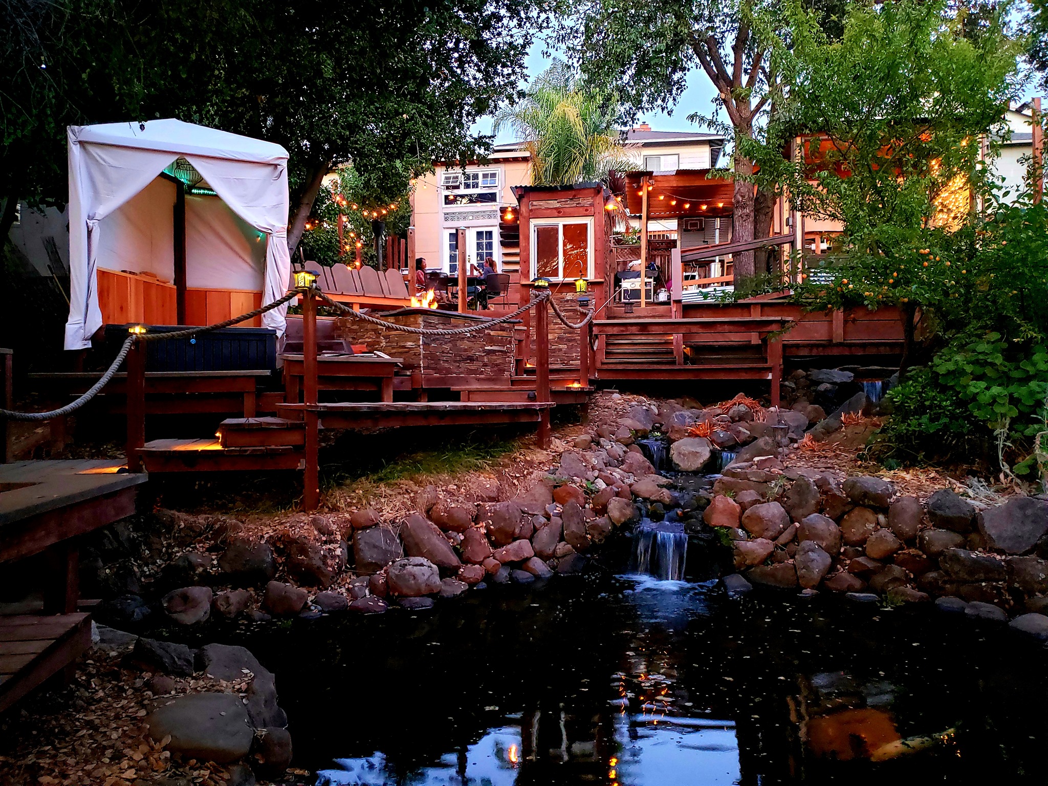 Outdoor patio with wooden walkways, string lights, and a small waterfall